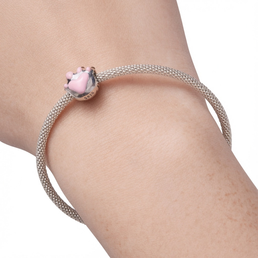 A silver pink paw print charm on bracelet worn on a woman's wrist, featuring a small pink paw-shaped charm with silver claws.