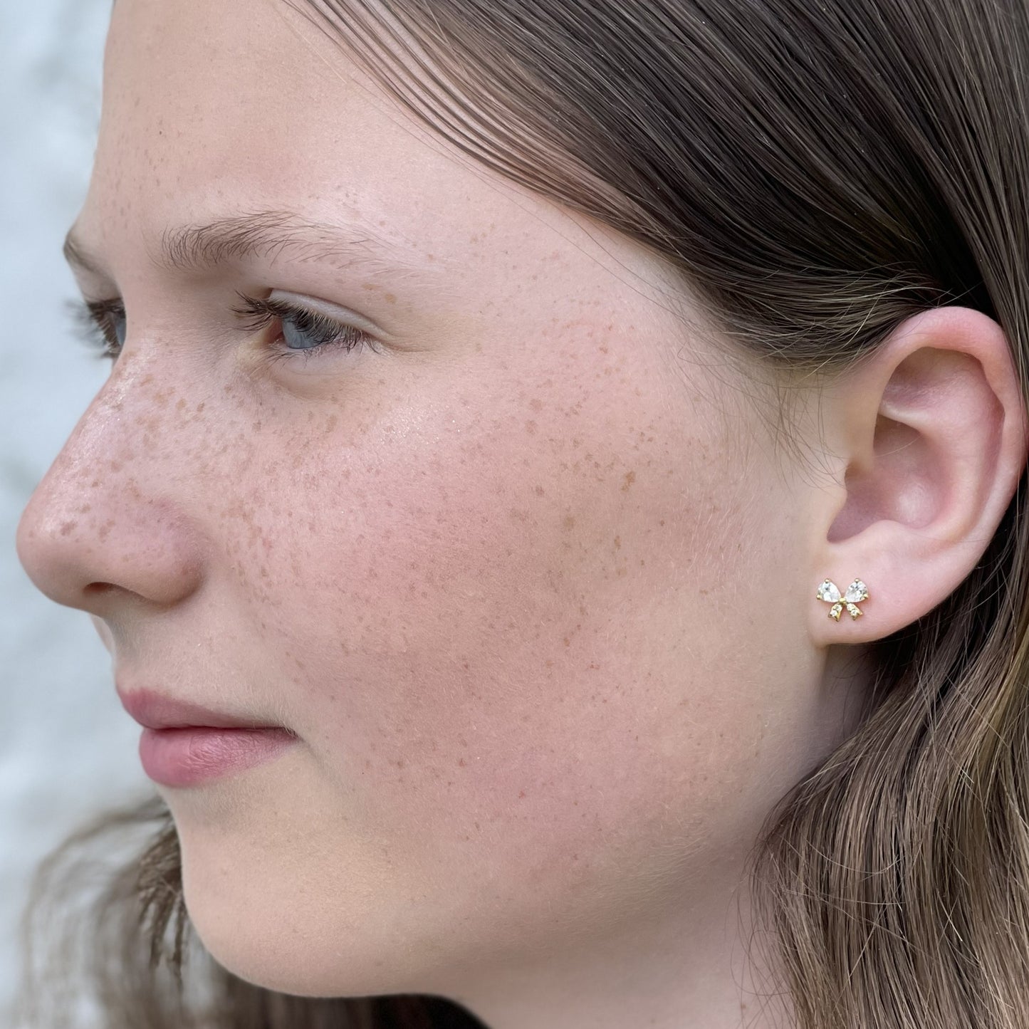 Close up of a woman wearing 925 sterling silver crystal bow stud earrings with zircon crystals on a white background