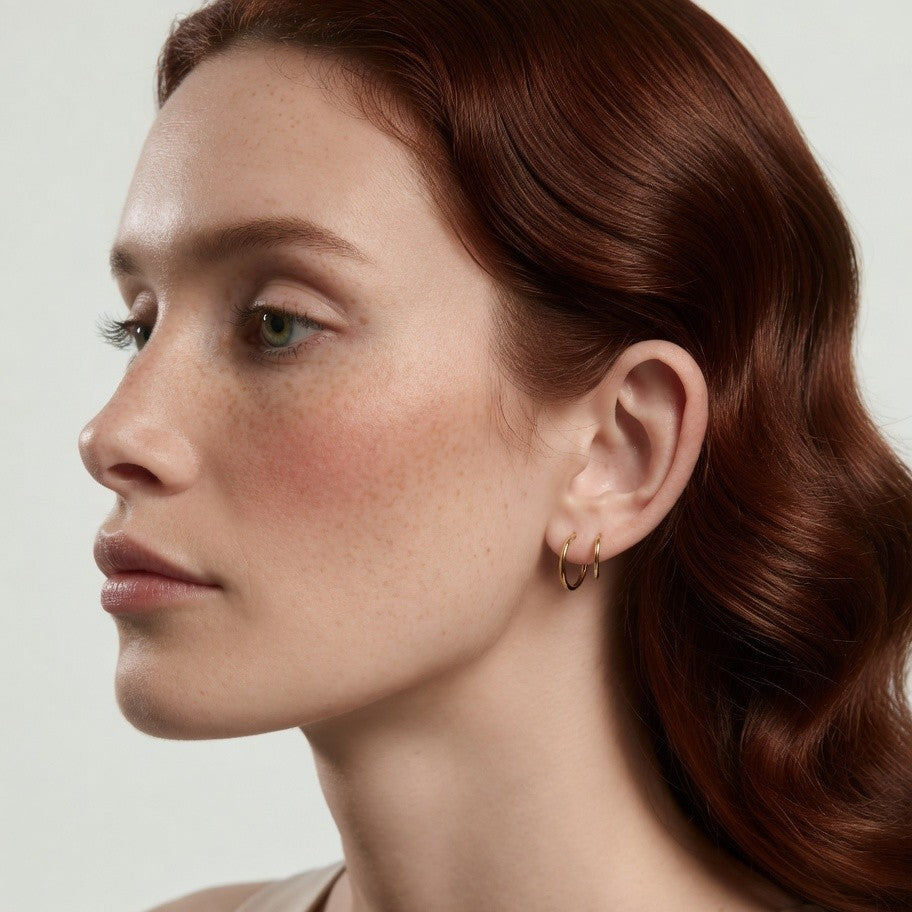 Close-up of a woman with red hair wearing a gold hoop earring on a light background