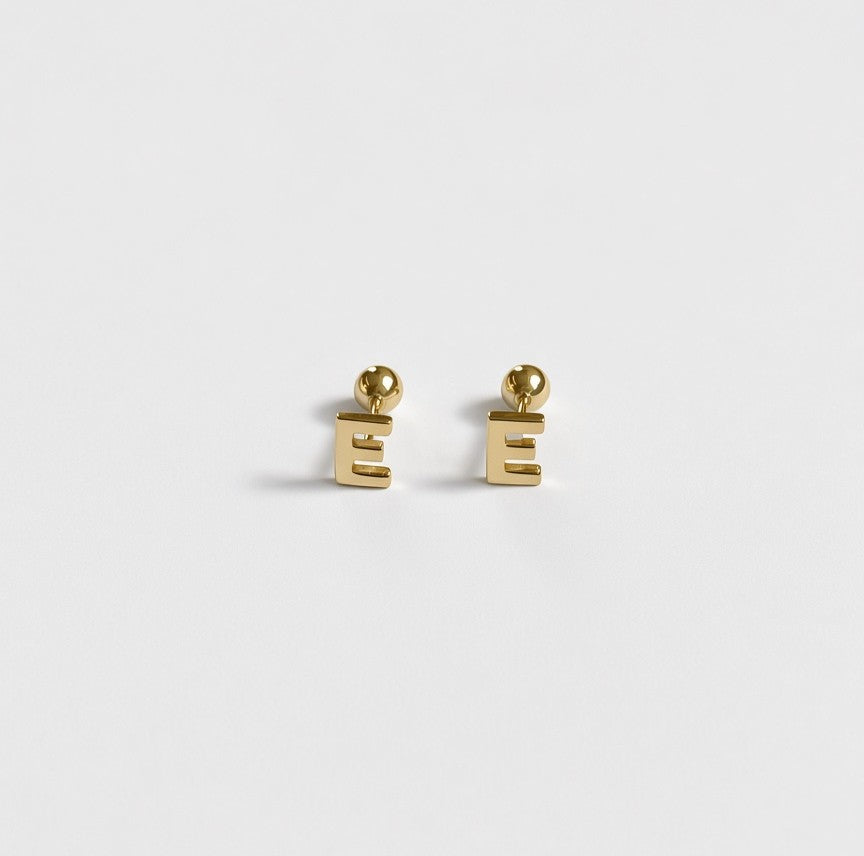 A pair of gold letter 'E' stud earrings on a clean, light gray background.
