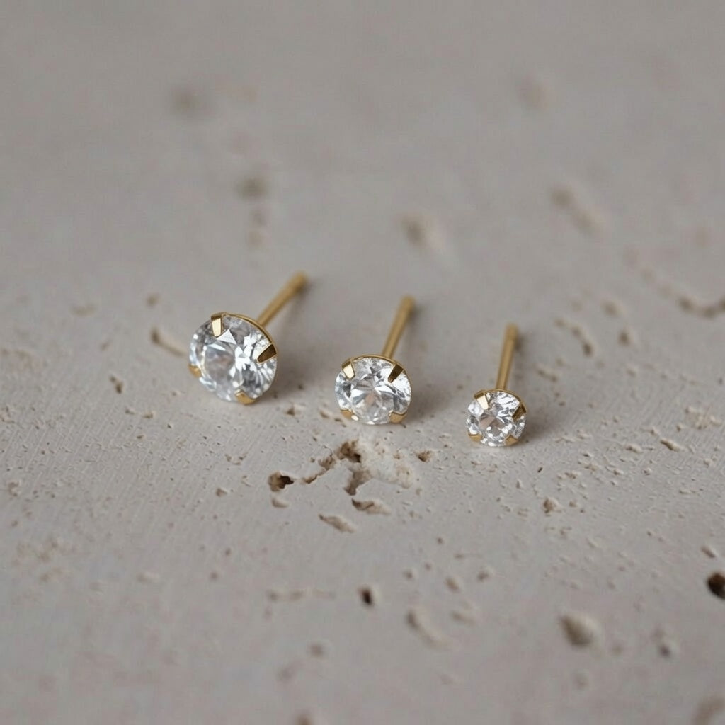 Three pairs of 14ct solid gold zircon stud earrings in 3mm, 4mm and 5mm sizes, showing the claw settings side by side on a neutral stone surface.