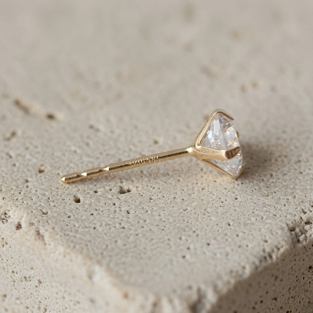 14ct solid gold zircon stud earring in 5mm size, showing the claw settings and post on a neutral stone surface.