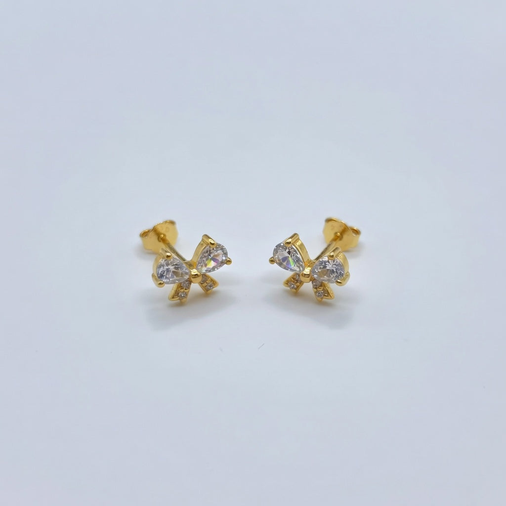 Gold crystal bow-shaped earrings with clear stones on a light gray background