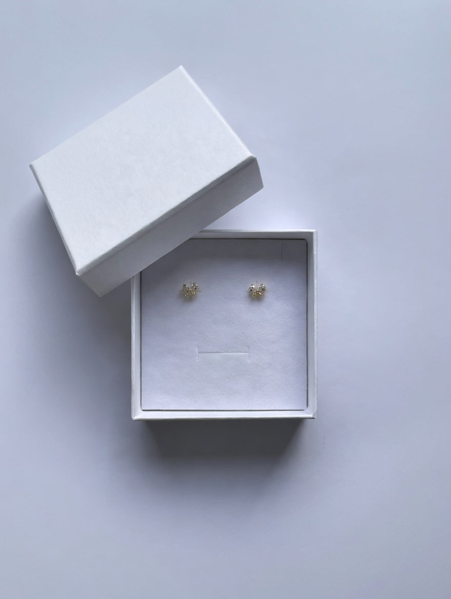 Gold crystal bow earrings in an open white box on a light gray background