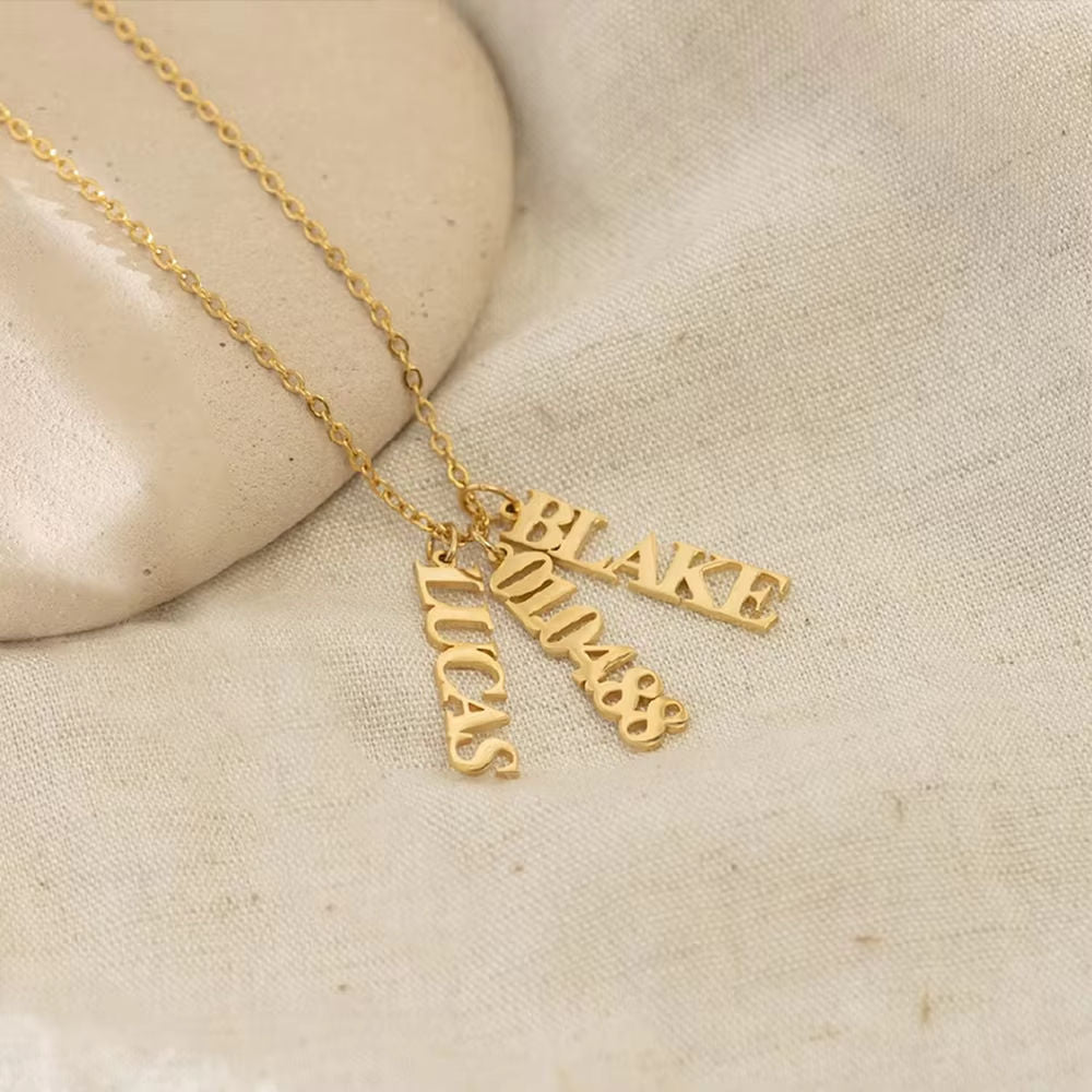 Gold necklace with three name pendants on a beige stone background