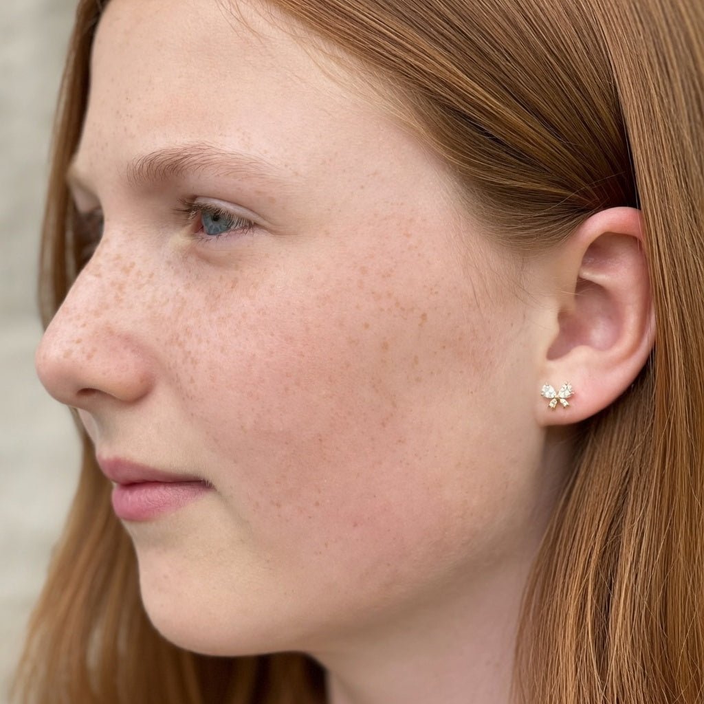Close-up of a female wearing small crystal bow earrings with a neutral background
