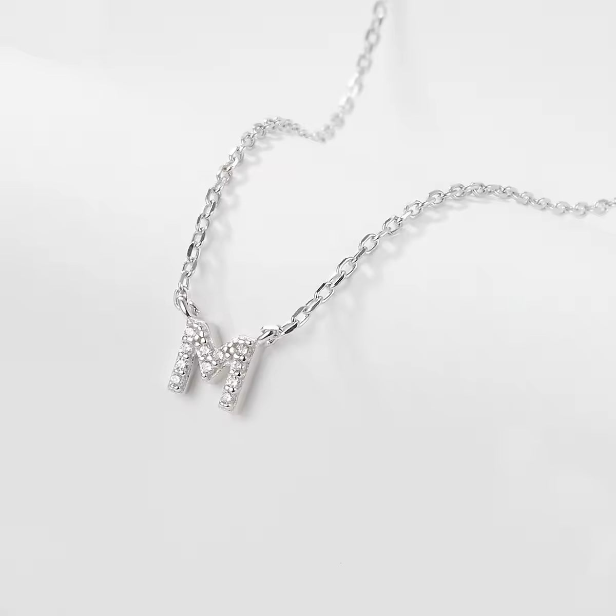 Silver necklace with a delicate zircon crystal M letter pendant on a light gray background