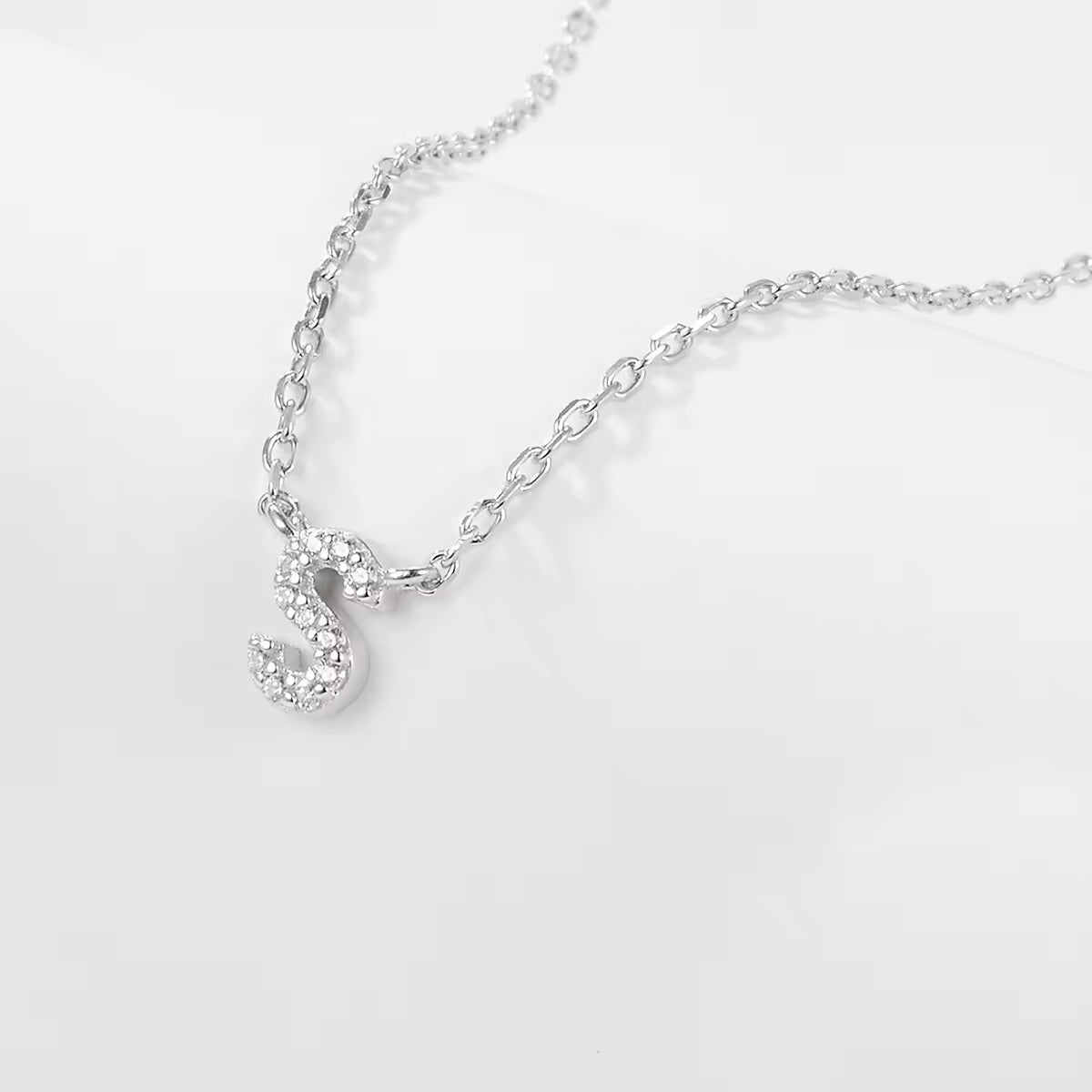 Silver necklace with a delicate zircon crystal S letter pendant on a light gray background