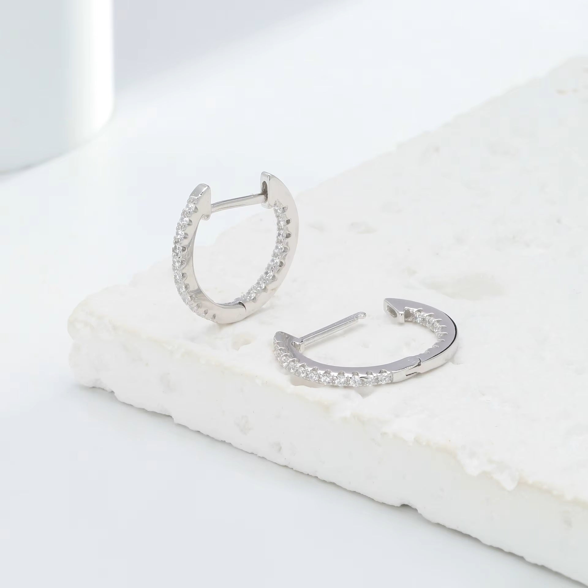 Sterling silver CZ hoop earrings showing open and closed click closure on white marble