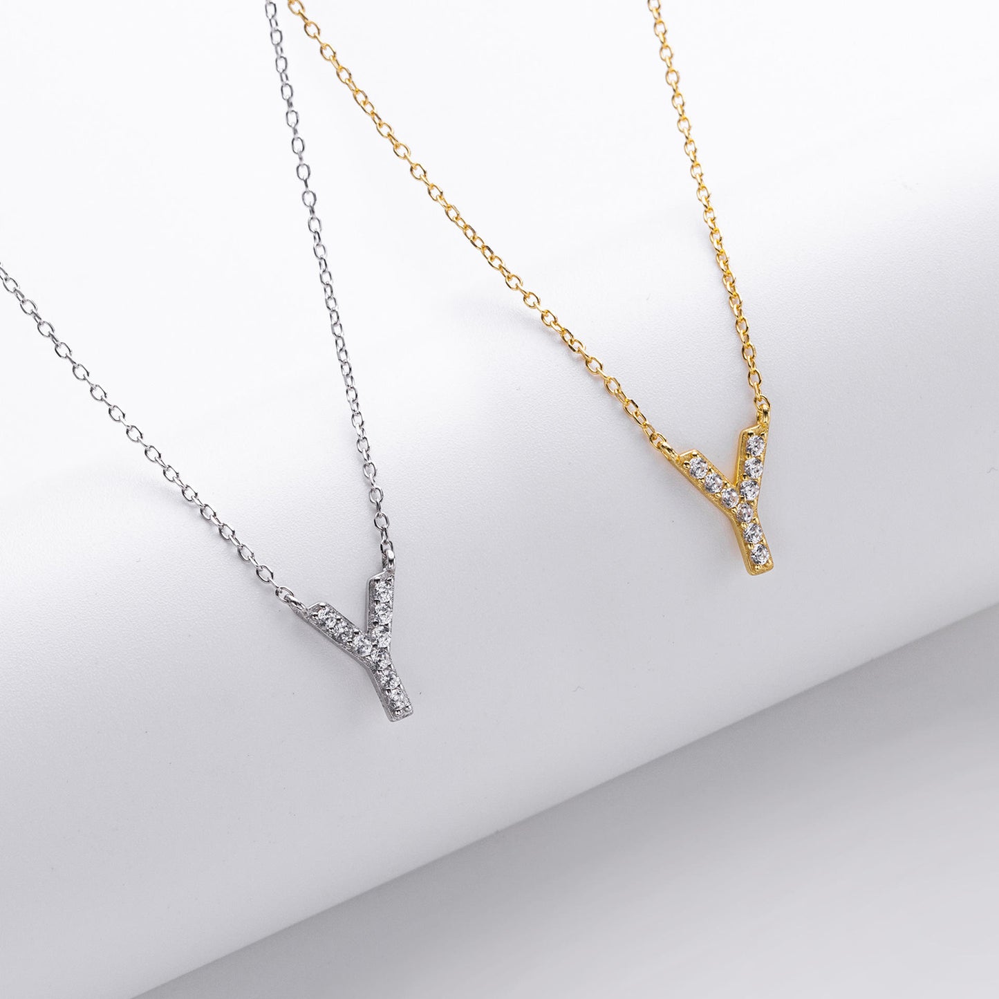 Two necklaces, one gold and one silver, with a 'V' initial letter on a light gray background.