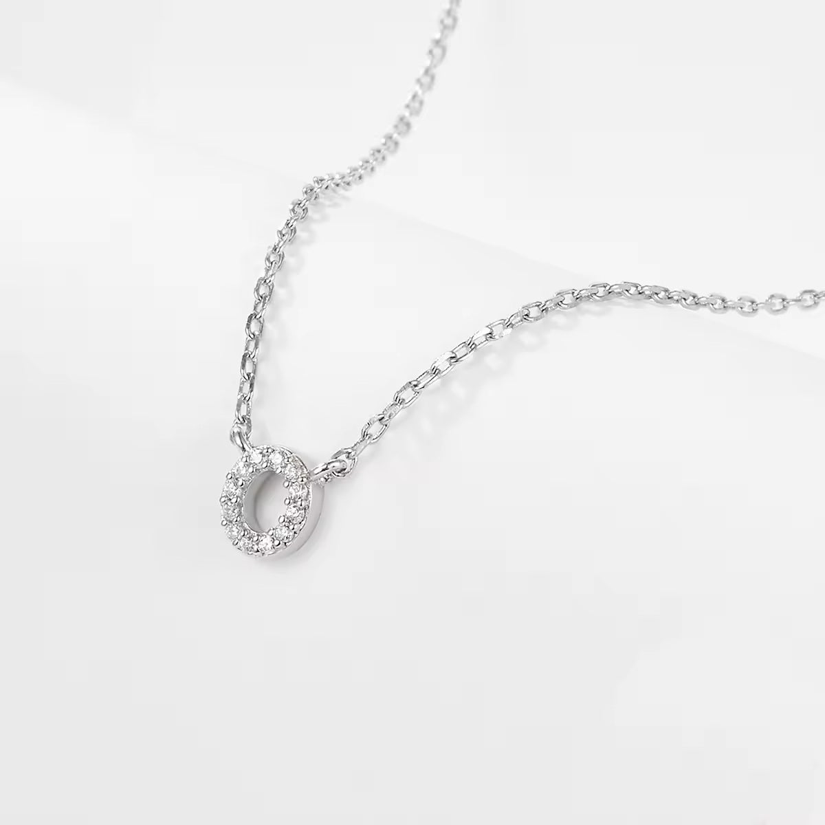 Silver necklace with a delicate zircon crystal O letter pendant on a light gray background