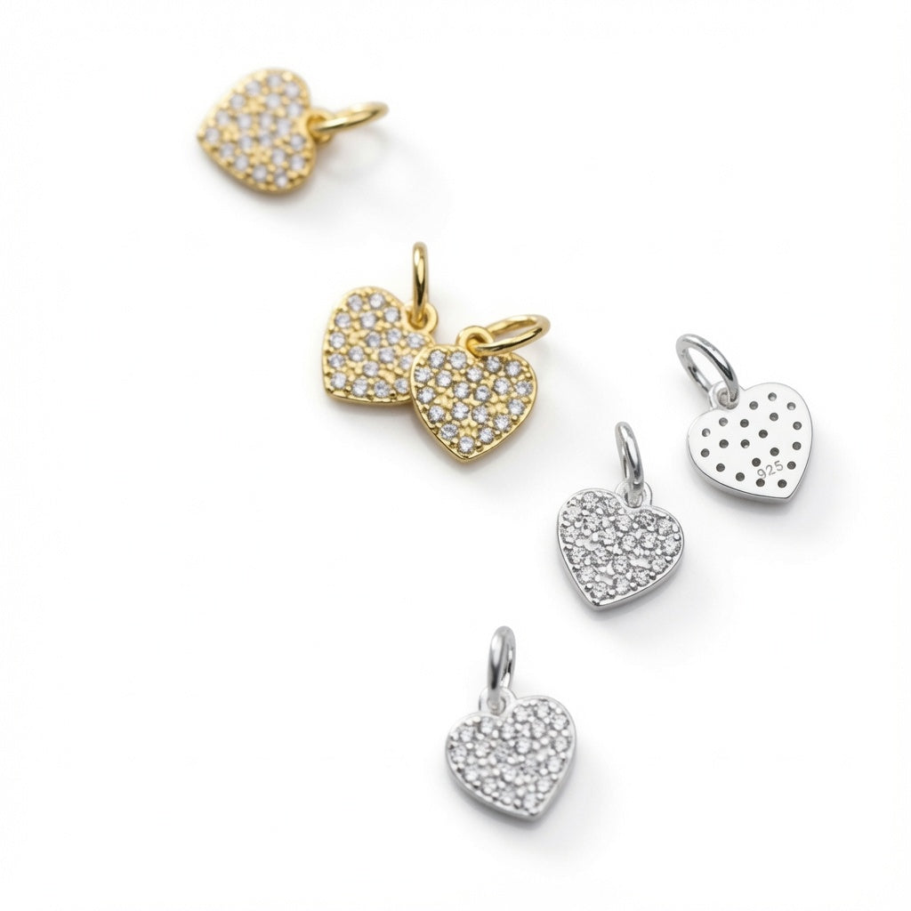 Five heart-shaped pavé charm pendants in gold and silver tones, arranged diagonally on a clean white background.
