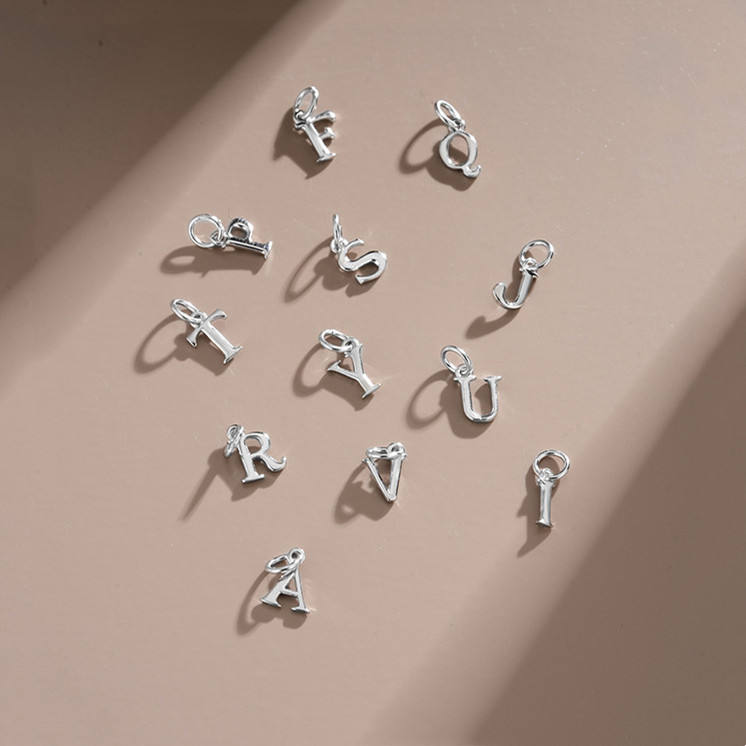 sterling Silver letter charm pendants on a beige background