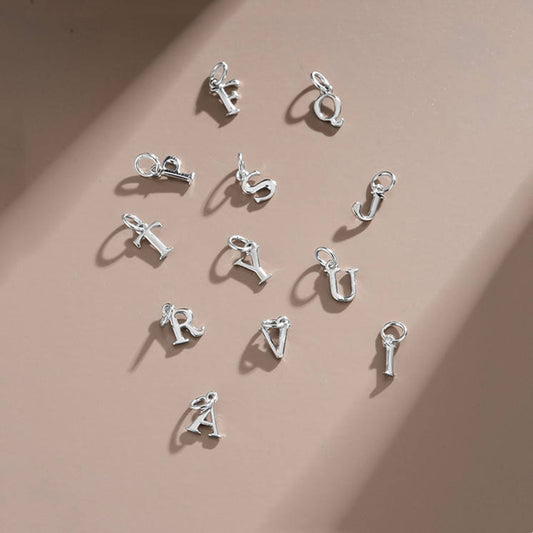 sterling Silver letter charm pendants on a beige background