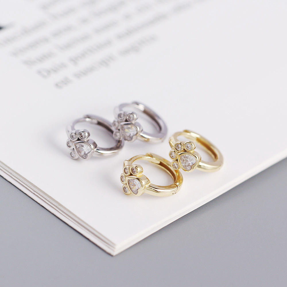Two sets of crystal paw print hoop earrings, one gold and one sterling silver, on a white surface.